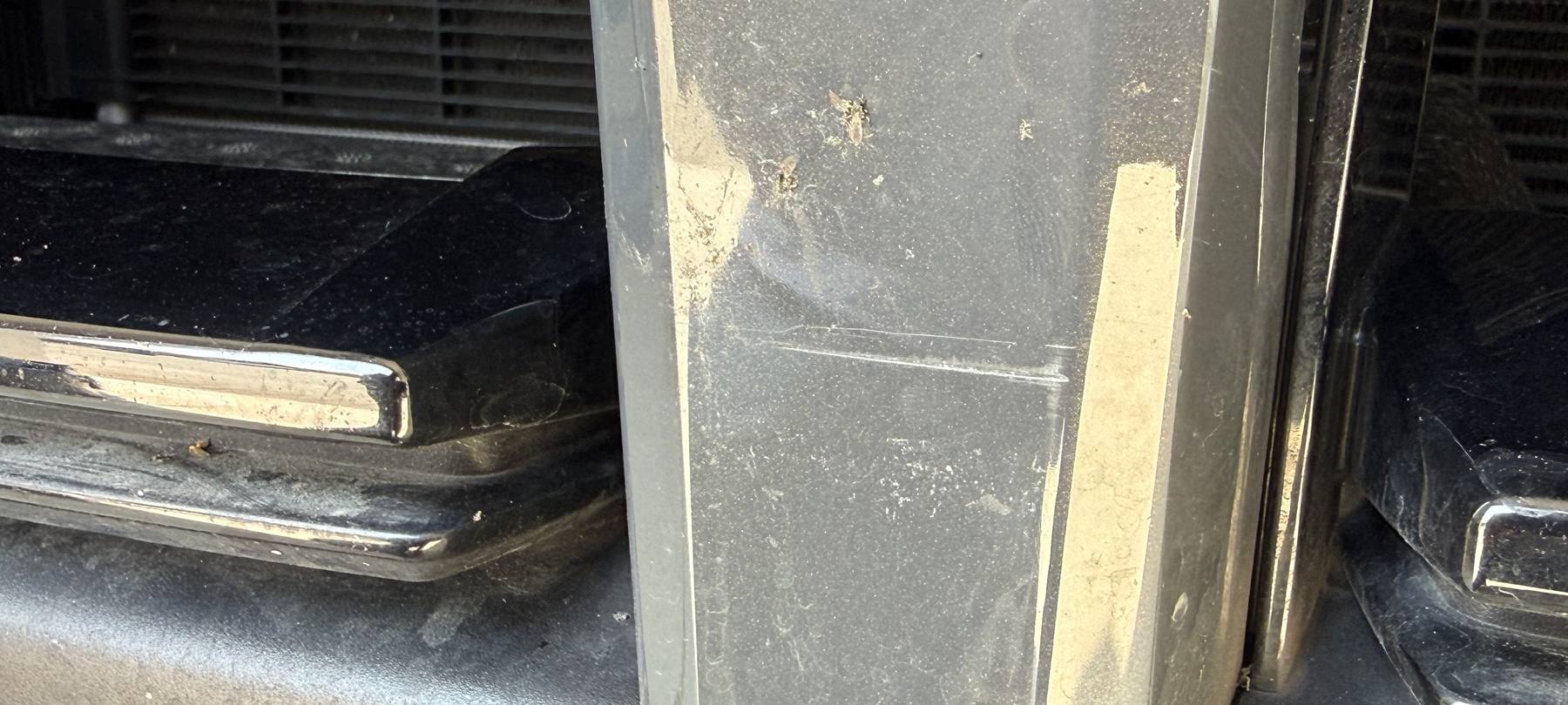 Aufgeschrammte Chromleiste am Kühlergrill eines dunkelgrauen BMW 3er, Nahaufnahme der Schadenstelle